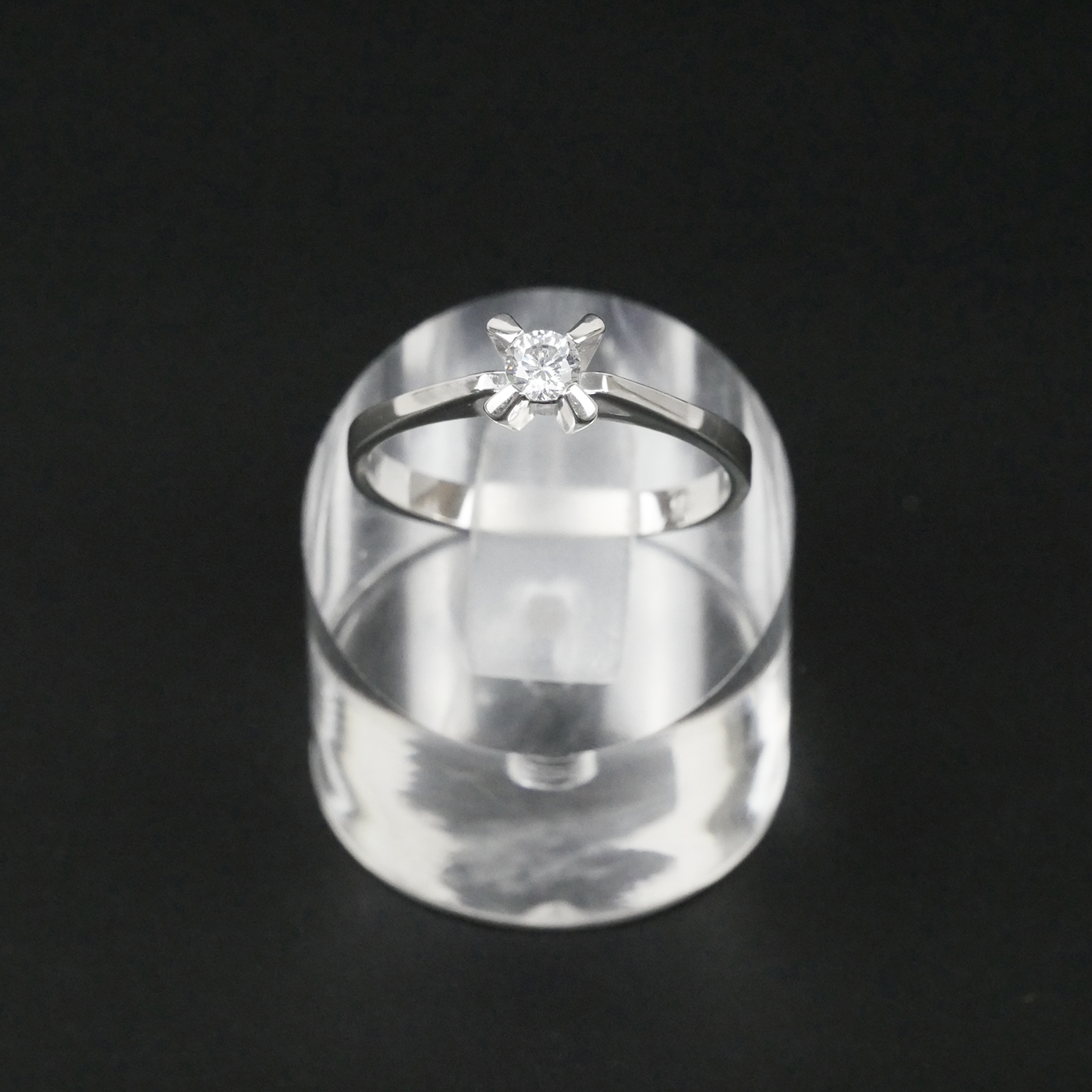Silver ring with a CZ on a clear stand against a black background