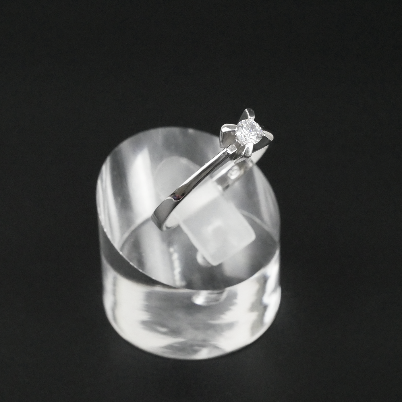 Silver ring with a star-shaped CZ on a clear stand against a black background