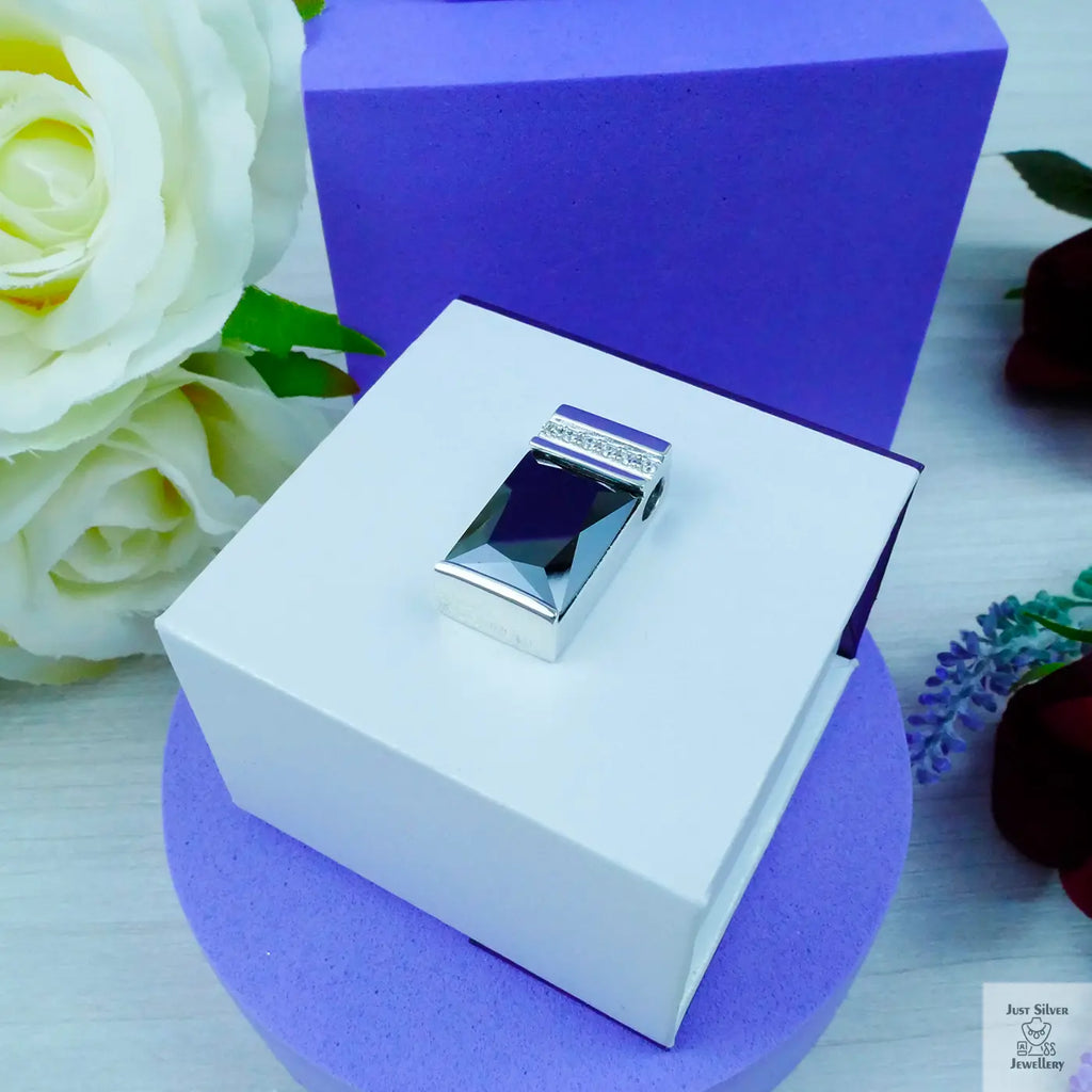 Silver ring in a white box with a purple background and flowers.