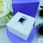Silver ring in a white box with a purple background and flowers.