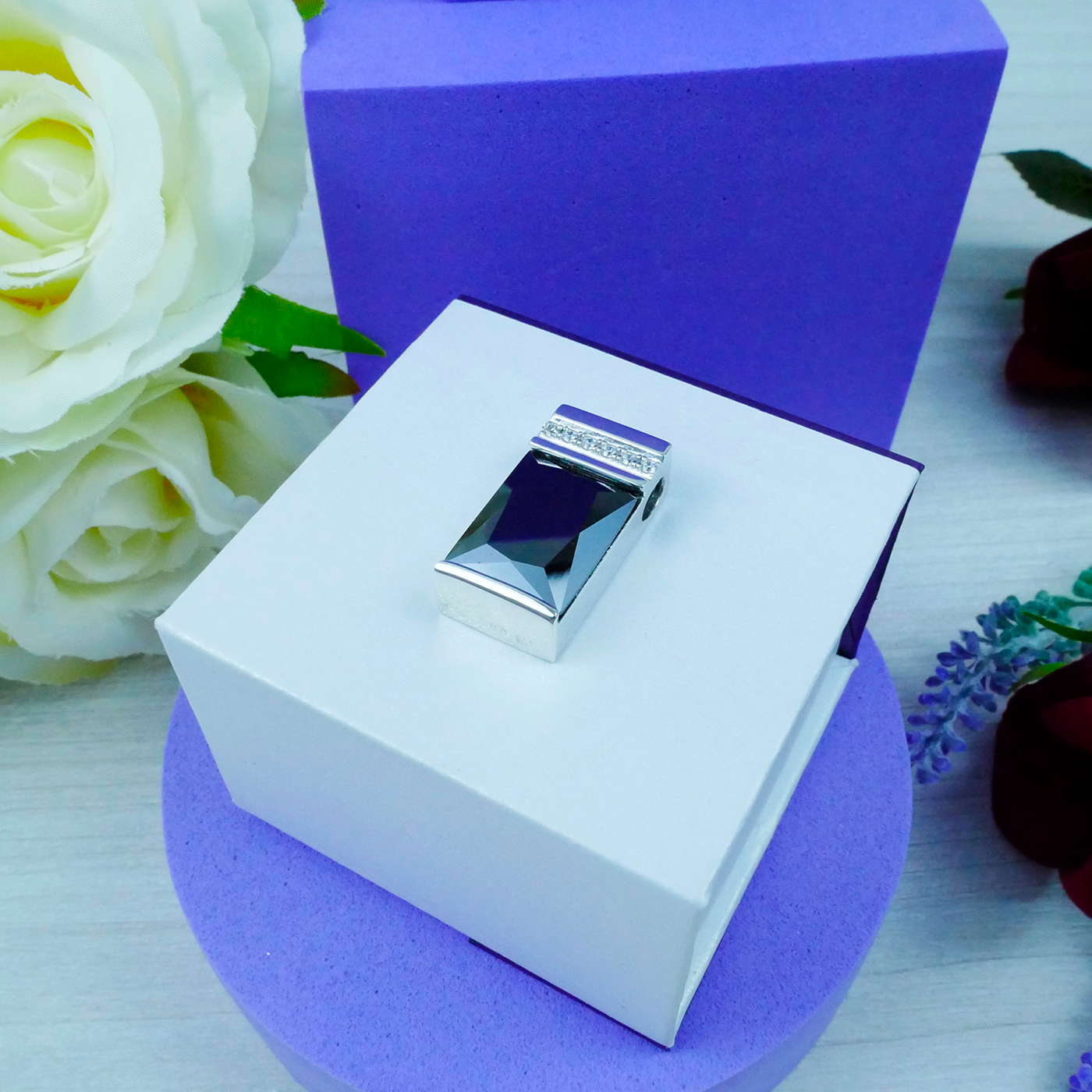 Silver ring in a white box with a purple background and flowers.