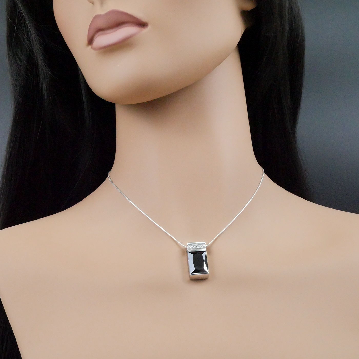 Mannequin wearing a silver necklace with a black pendant on a dark background