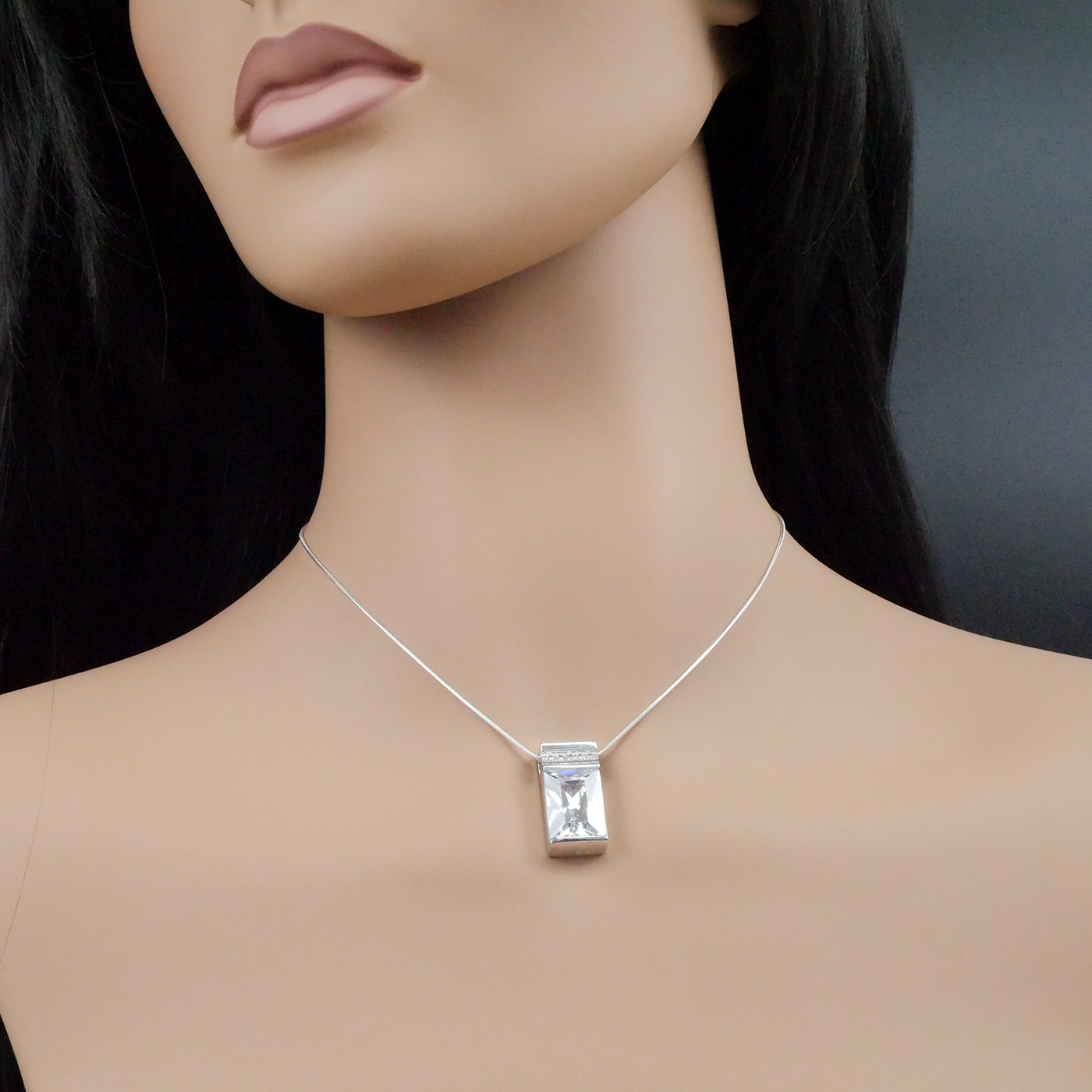 Mannequin wearing a silver necklace with a rectangular pendant on a dark background