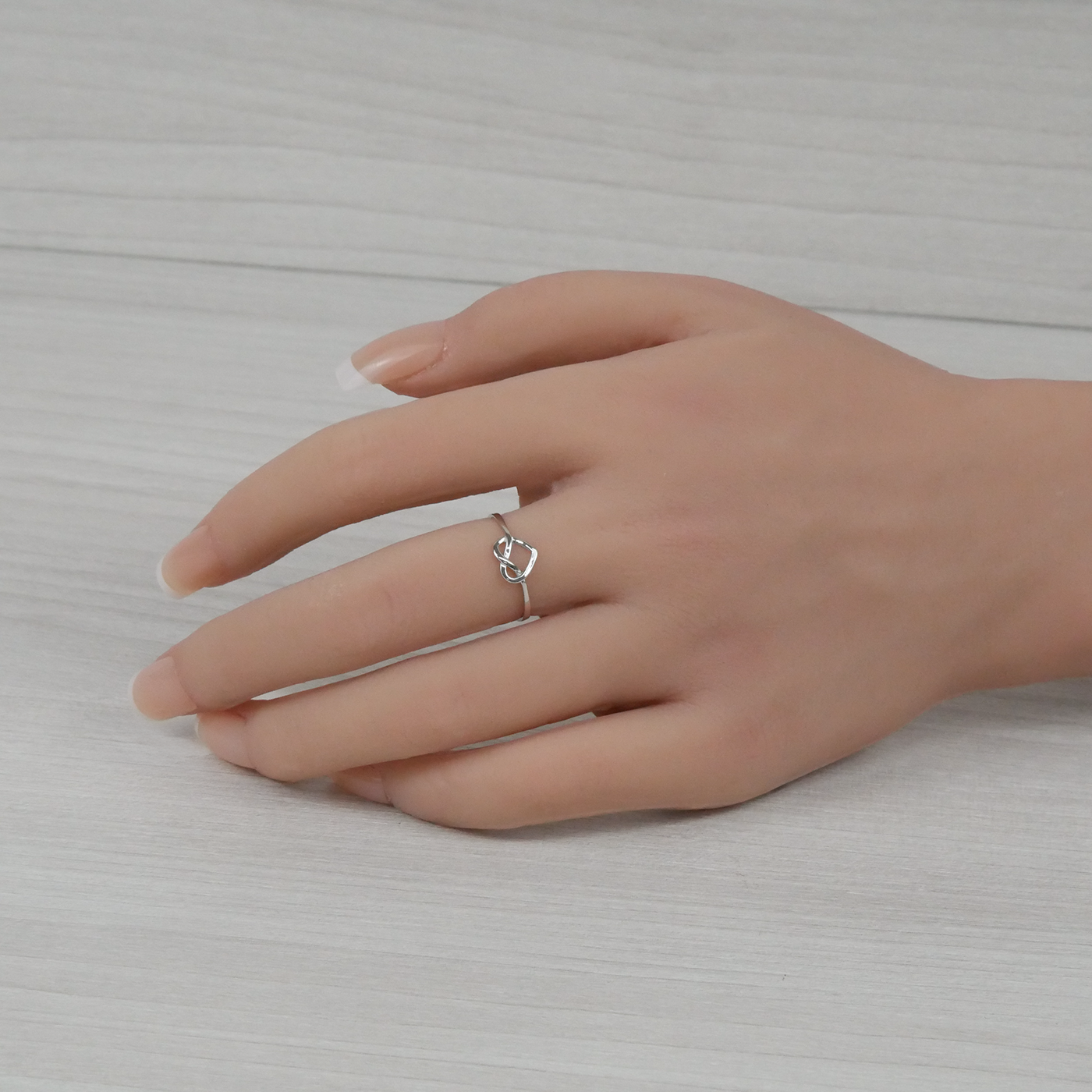 Hand wearing a silver ring on a neutral background