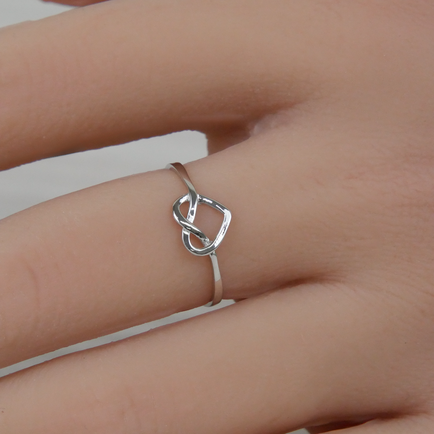 Silver knot ring on a person's finger against a neutral background