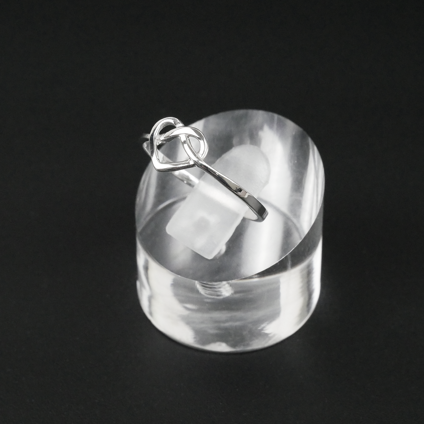 Silver ring with a heart design on a clear stand against a black background