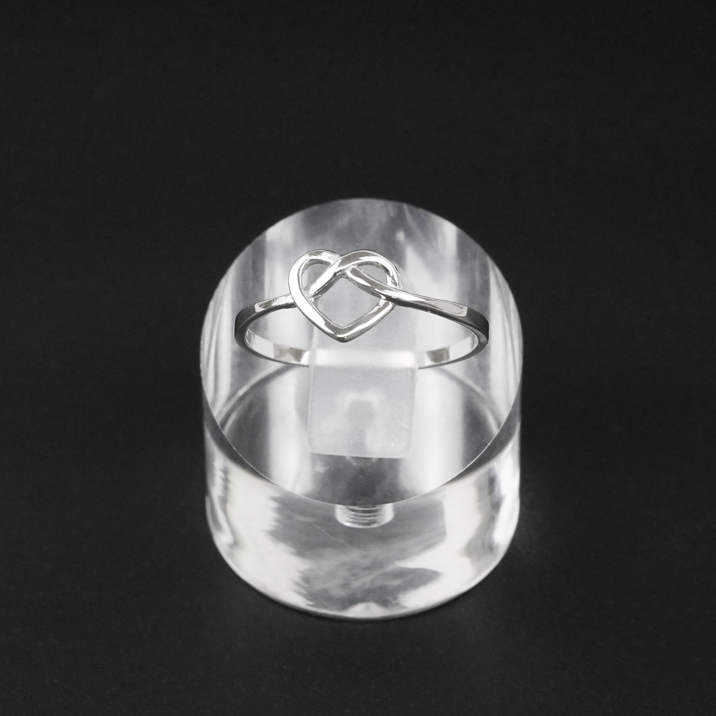 Silver ring with a heart design on a clear stand against a black background