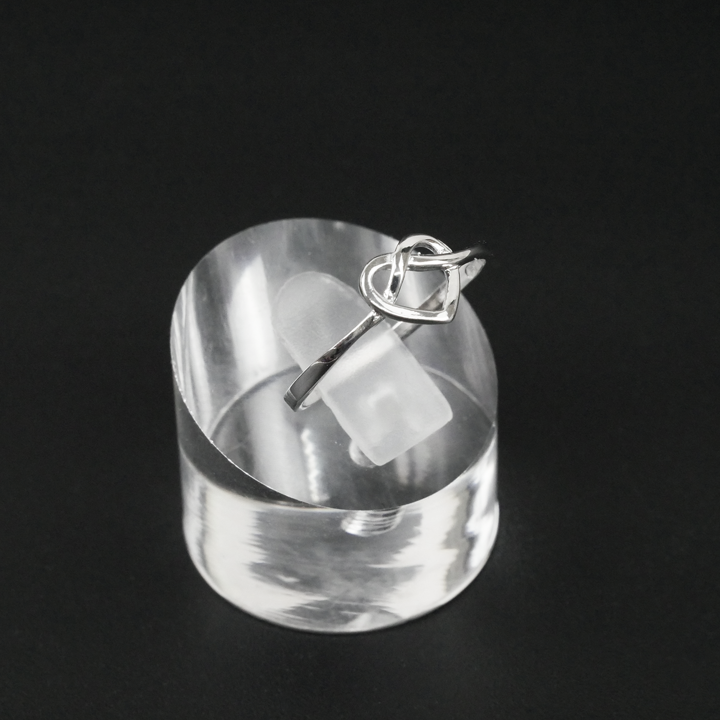 Silver ring with a heart design on a clear stand against a black background