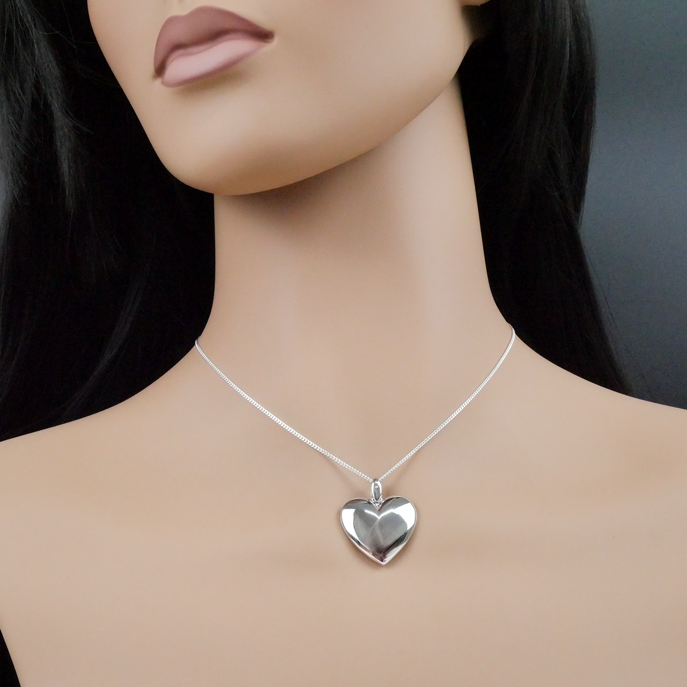 Mannequin wearing a silver heart-shaped necklace on a plain background