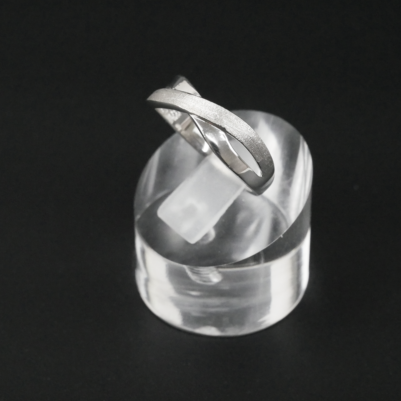 Silver two-tone ring on a clear crystal block against a black background