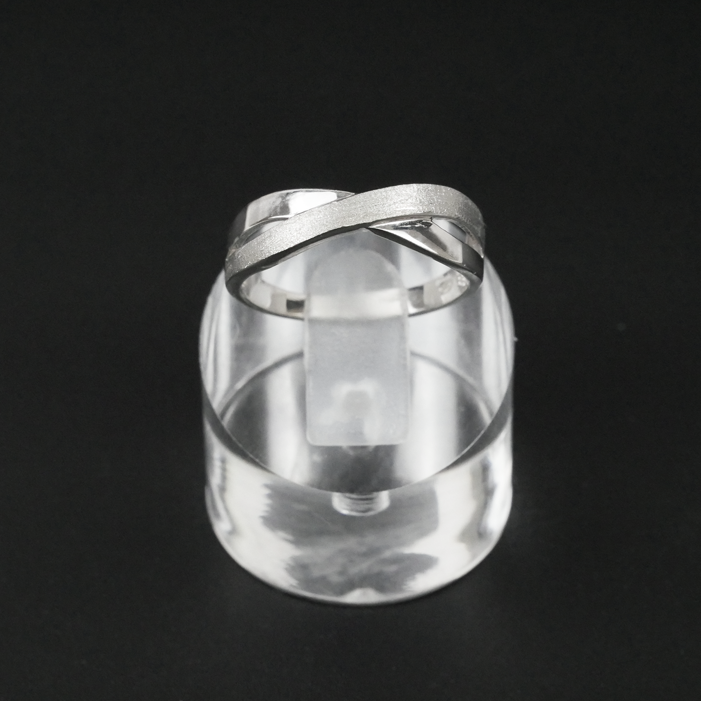 Silver two-tone ring on a clear crystal block against a black background