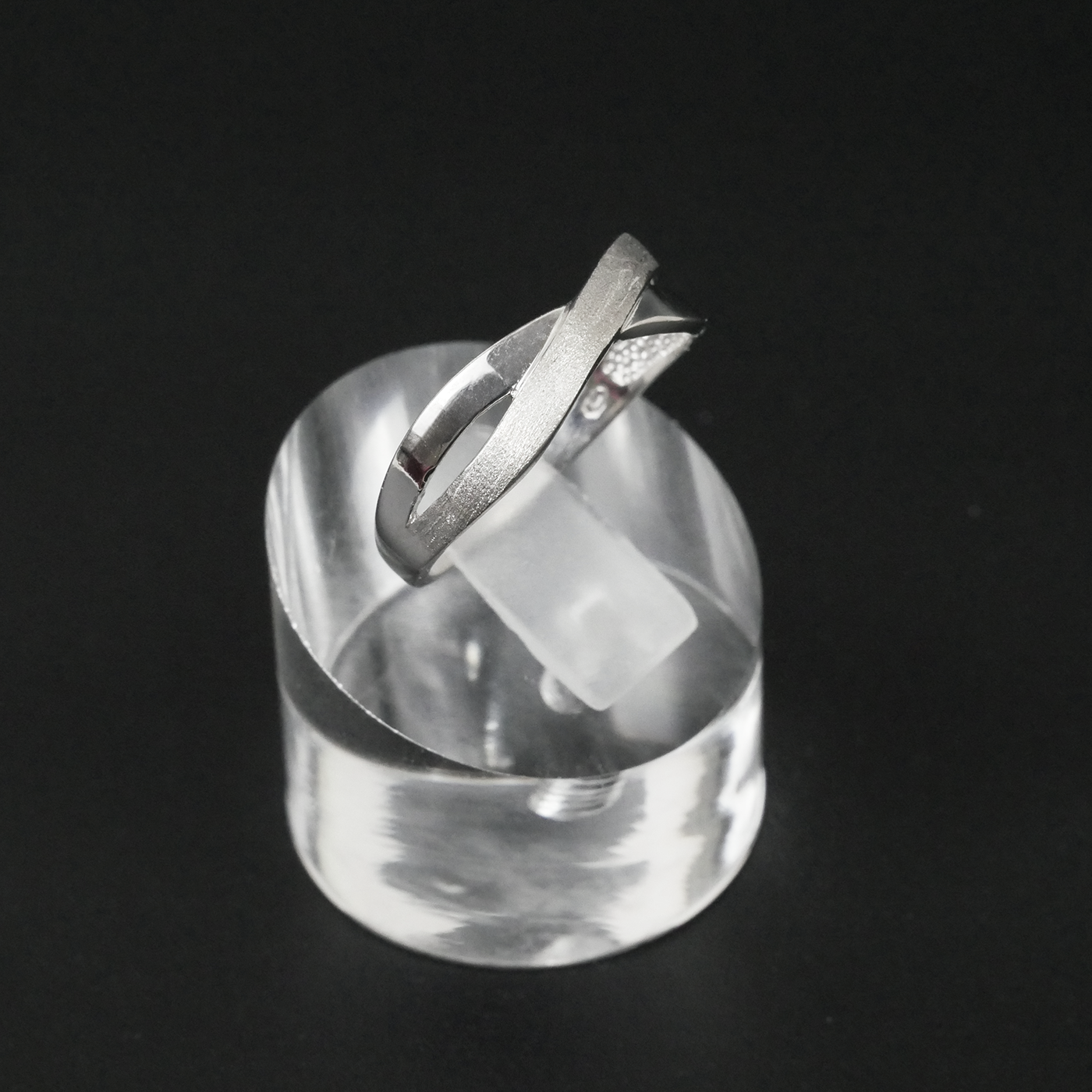 Silver two-tone ring on a clear crystal block against a black background