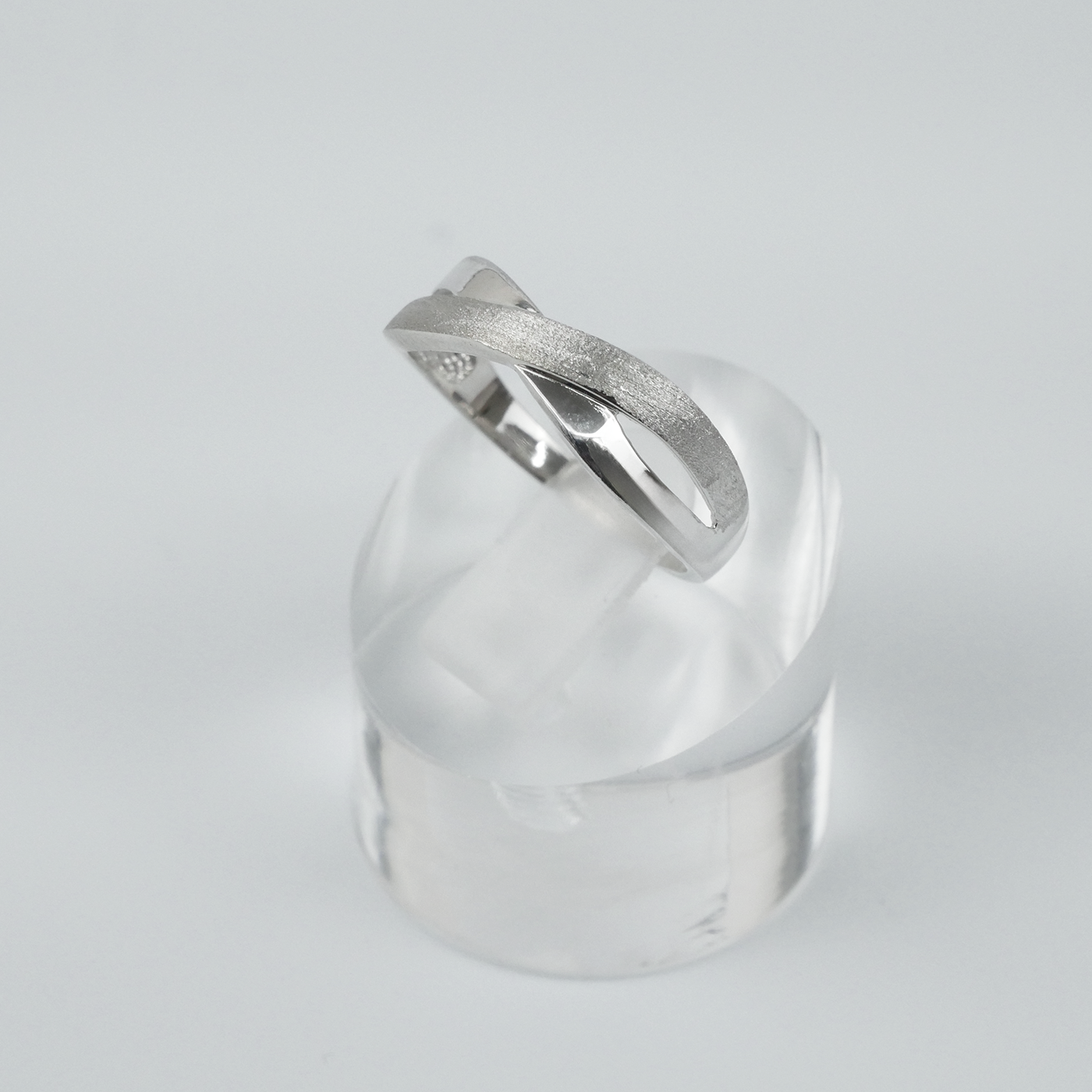 Silver two-tone ring on a clear crystal block against a light grey background