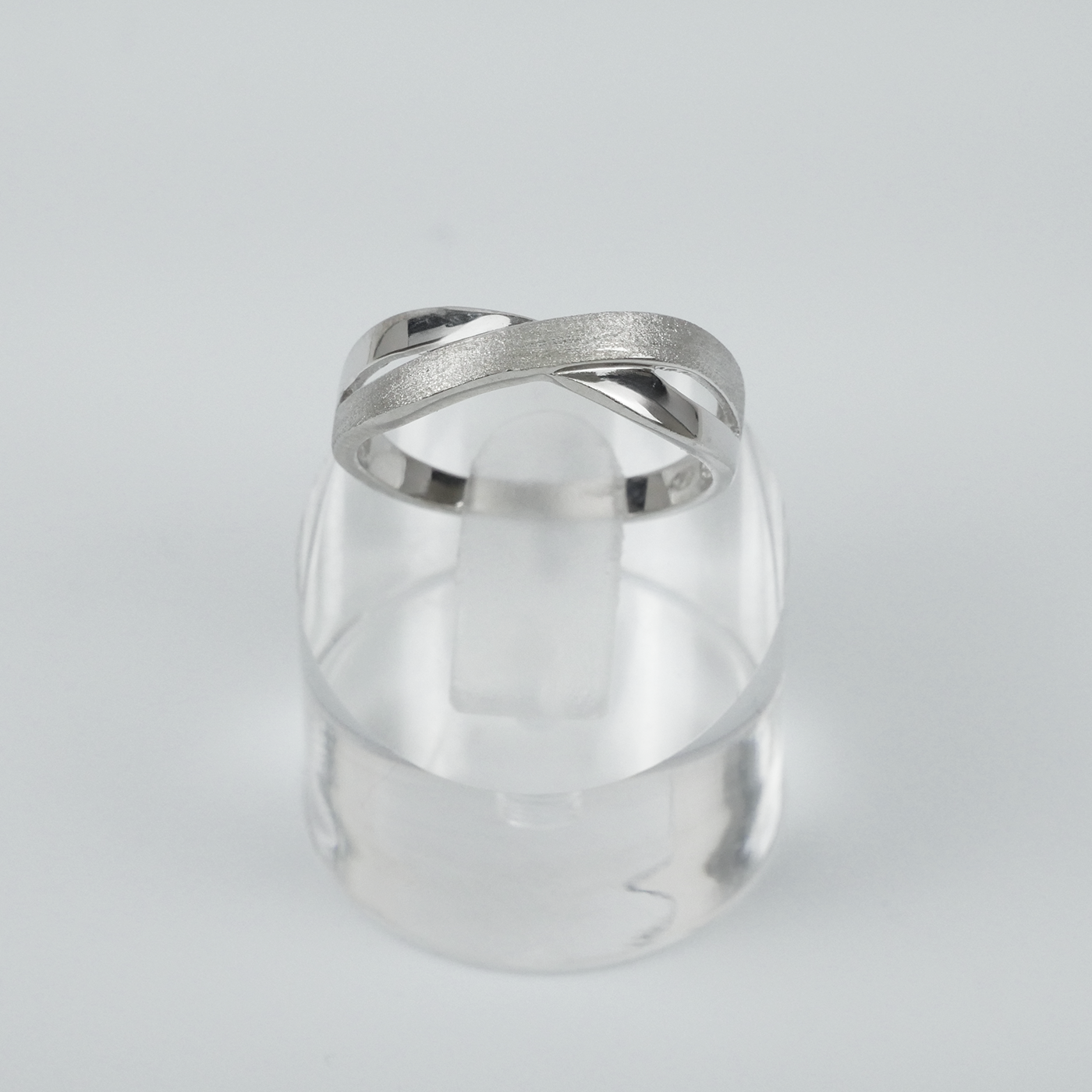 Silver two-tone ring on a clear crystal block against a light grey background