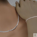 Silver marina chain necklace and bracelet on a person's wrist against a neutral background