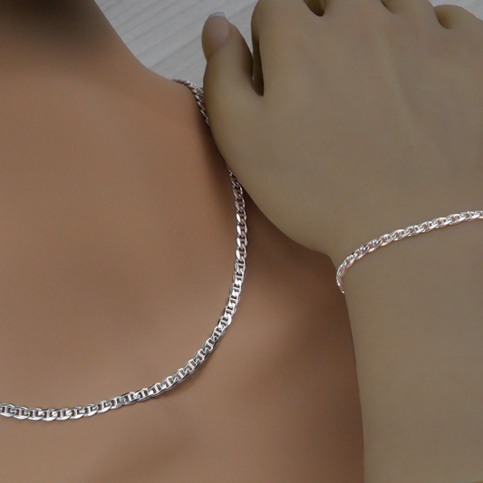 Silver marina chain necklace and bracelet on a person's wrist against a neutral background