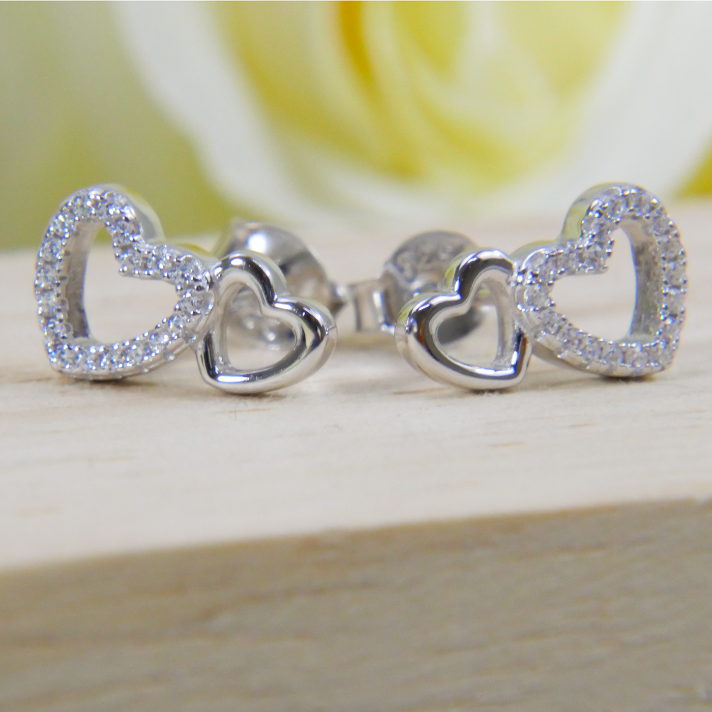 Silver heart-shaped earrings on a wooden surface with a blurred yellow rose in the background