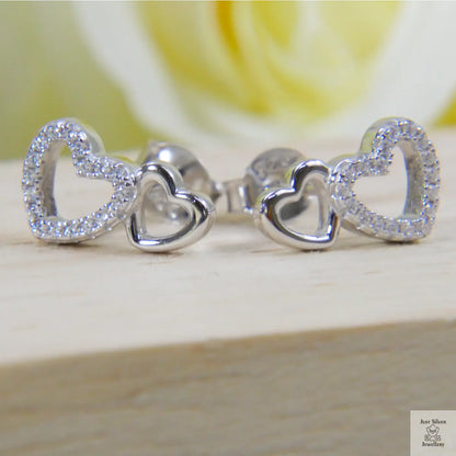Silver heart-shaped earrings on a wooden surface with a blurred yellow rose in the background