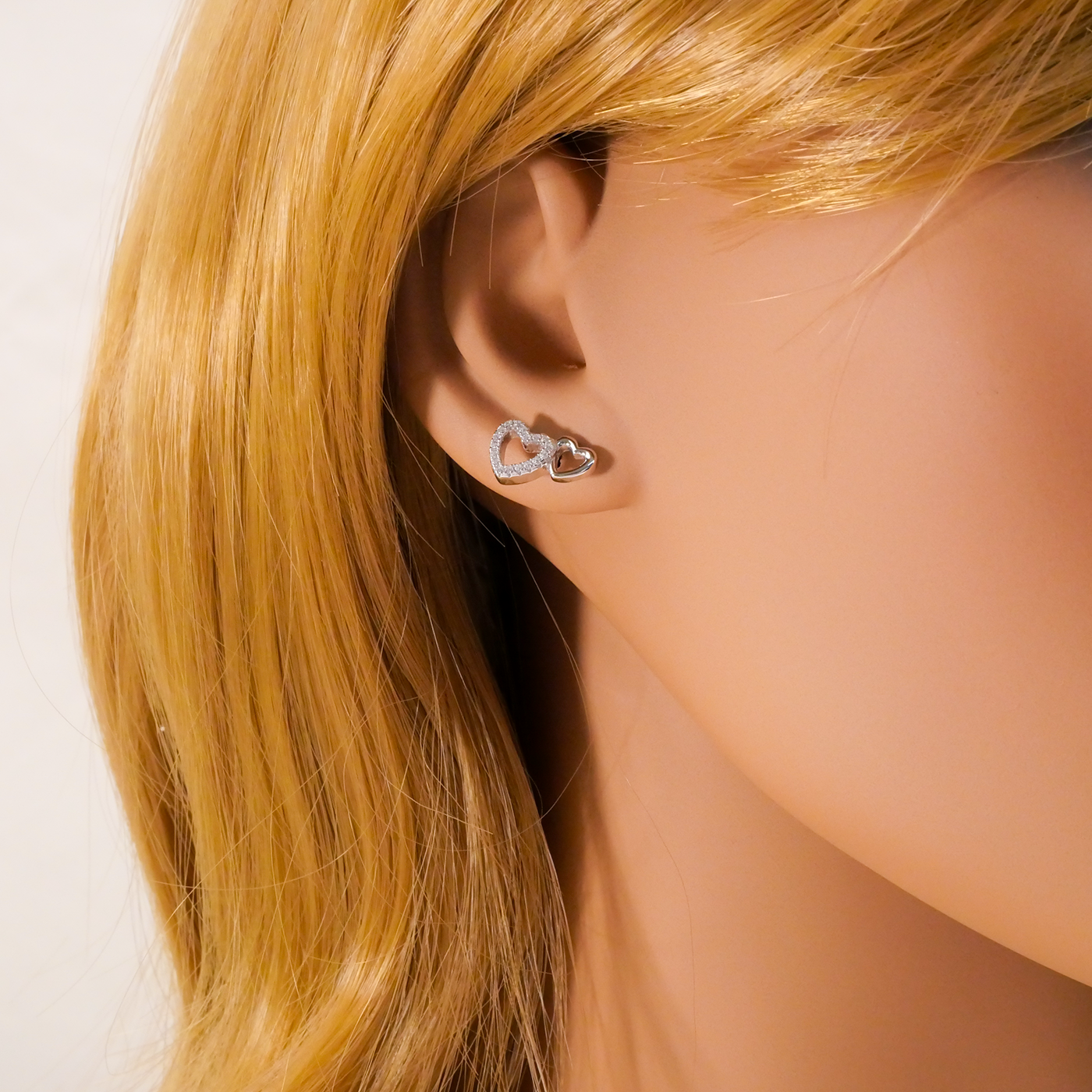 Close-up of an ear wearing a heart-shaped earring with blonde hair.