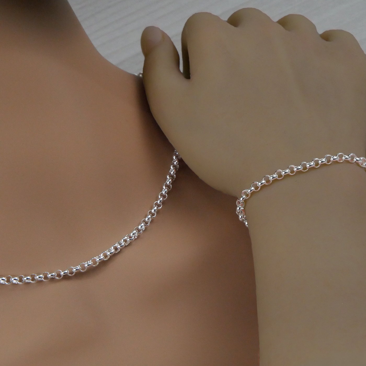 Silver rolo necklace and bracelet on a person's neck and wrist against a neutral background