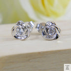 Silver earrings with a central zircon gemstone on a wooden surface with a blurred yellow flower in the background