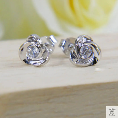 Silver earrings with a central zircon gemstone on a wooden surface with a blurred yellow flower in the background