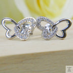 Silver butterfly-shaped earrings on a wooden surface with a blurred yellow flower in the background