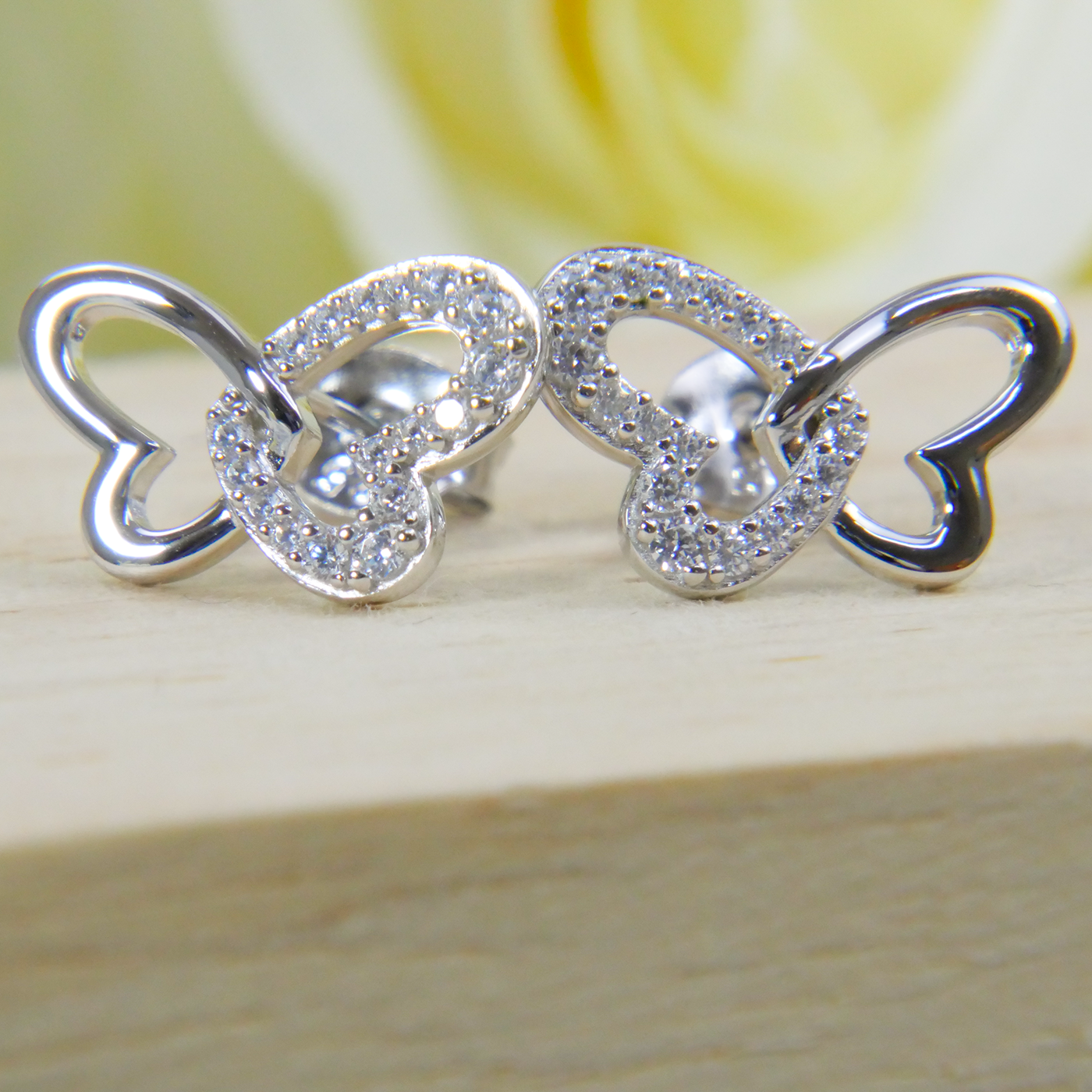 Silver butterfly-shaped earrings on a wooden surface with a blurred yellow flower in the background