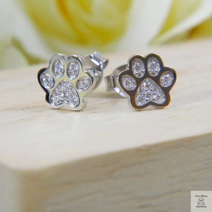 Paw print earrings with clear zircon stones on a wooden surface with a blurred floral background