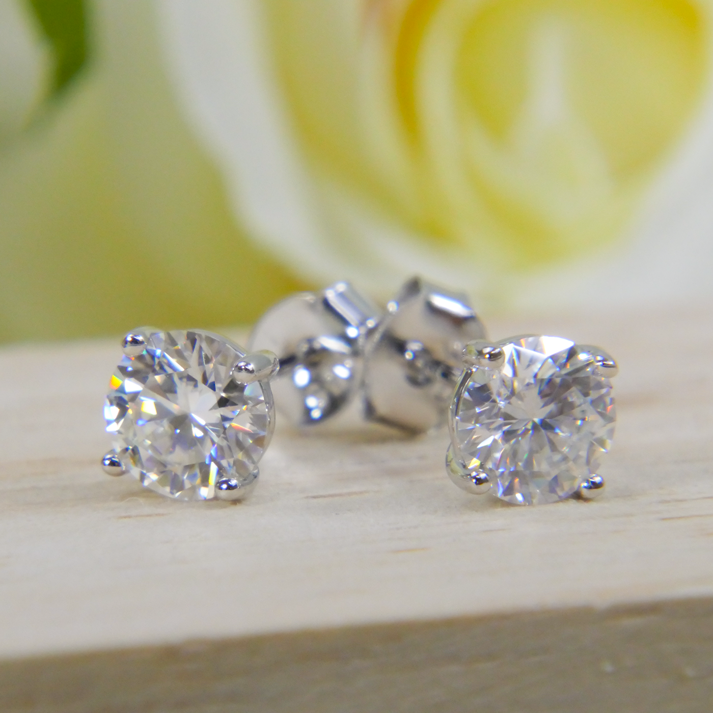 Natural Zircon stud earrings on a wooden surface with a blurred yellow flower in the background