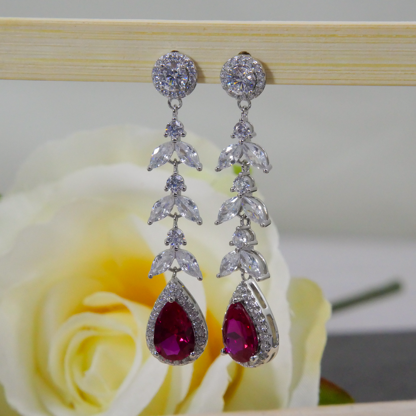 Silver earrings with red zircon gemstones on a wooden stand with a rose in the background
