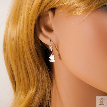 Close-up of a woman wearing a silver smiling cat earring against a neutral background.