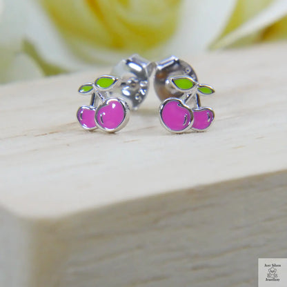 Cherry-themed stud earrings on a wooden surface with a blurred floral background