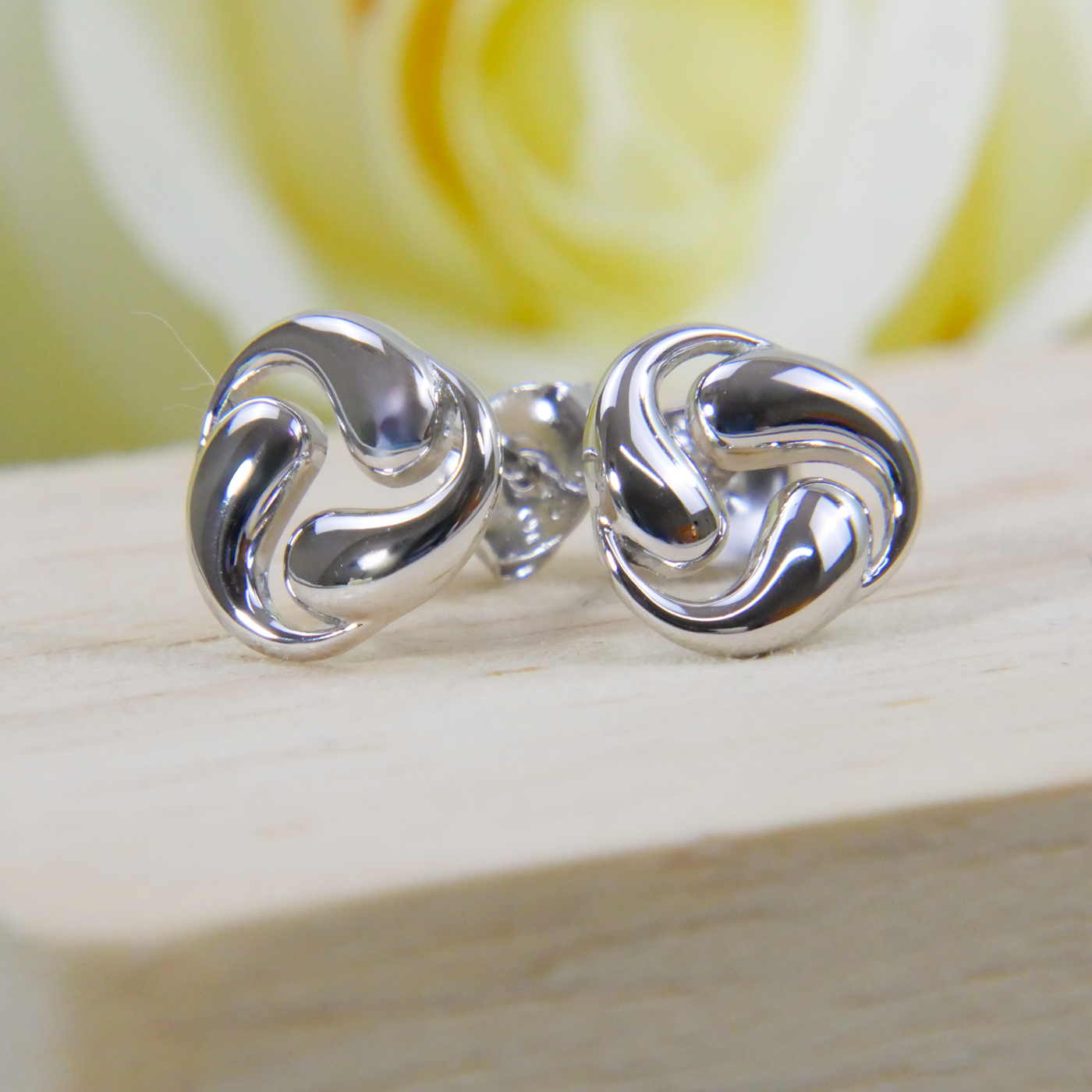 Silver swirl earrings on a wooden surface with a blurred yellow flower in the background