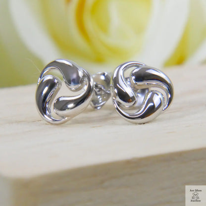 Silver swirl earrings on a wooden surface with a blurred yellow flower in the background
