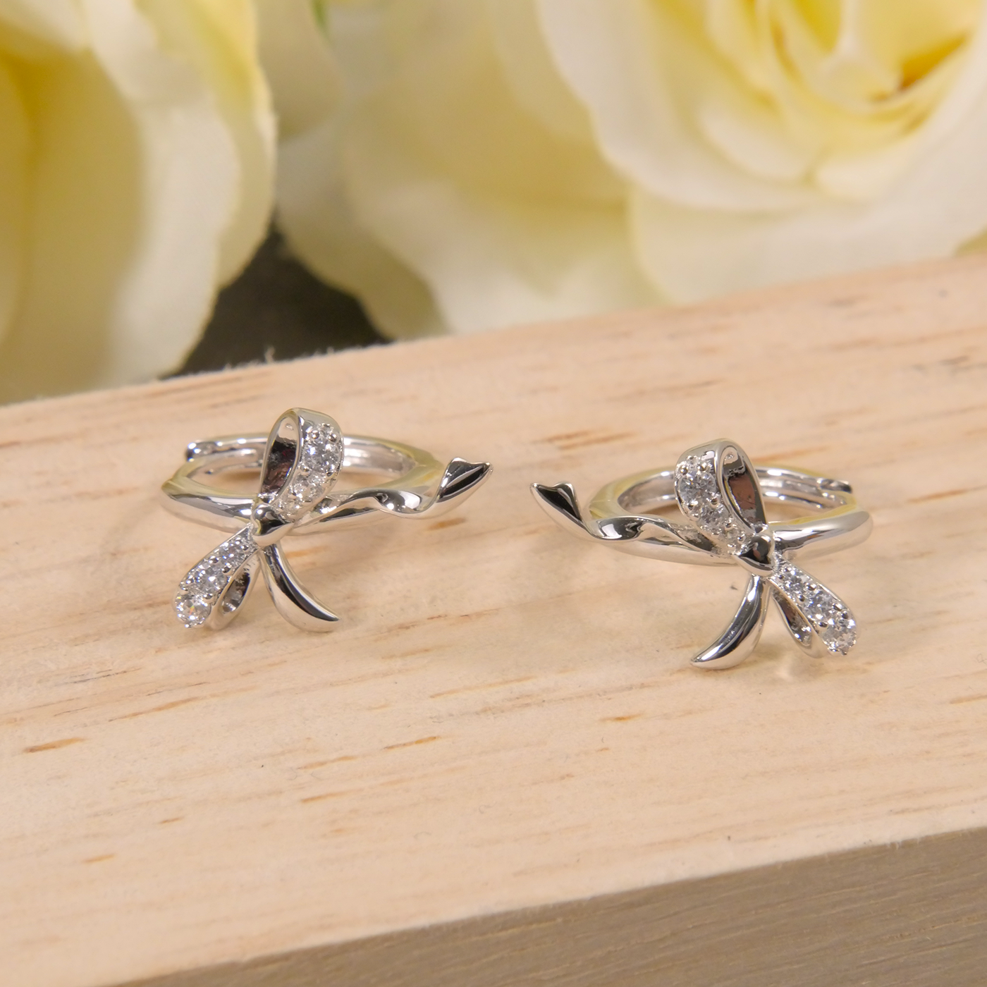 Two silver bow-shaped rings on a wooden surface with yellow roses in the background