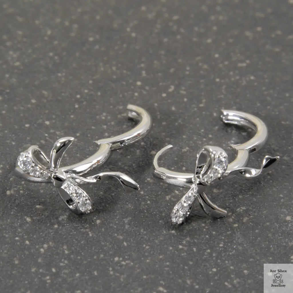 Silver bow-shaped earrings with clear stones on a gray surface