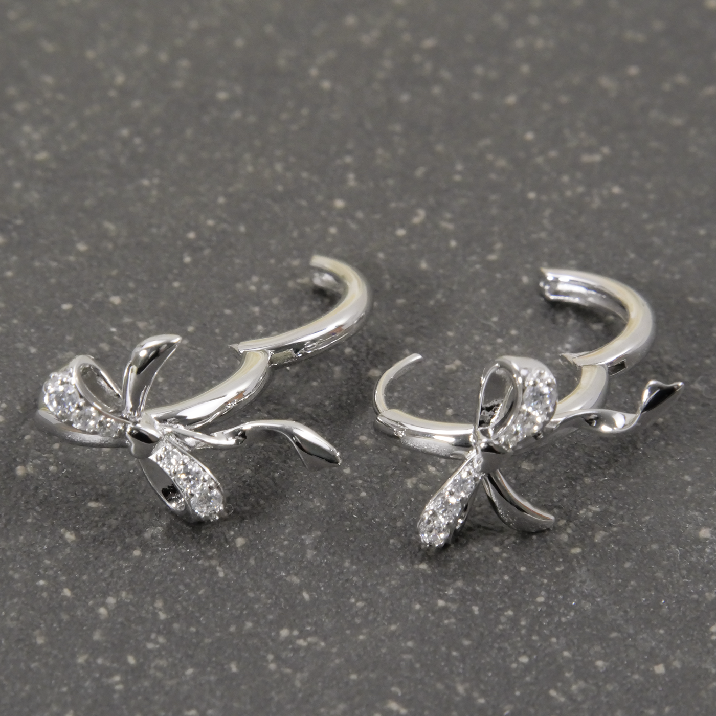 Silver bow-shaped earrings with clear stones on a gray surface