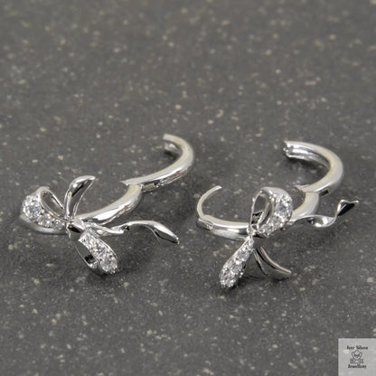 Silver bow-shaped earrings with clear stones on a gray surface