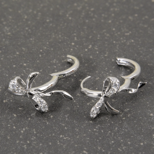 Silver bow-shaped earrings with clear stones on a gray surface