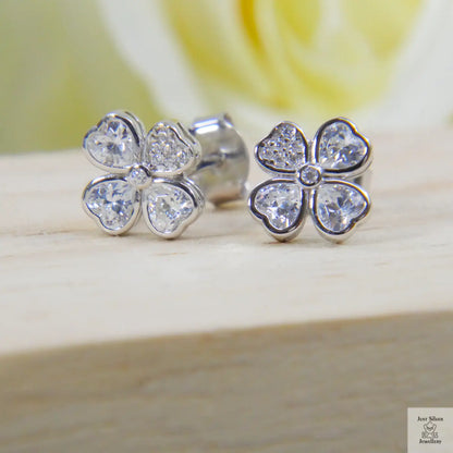 Silver four-leaf clover earrings with clear gemstones on a wooden surface.