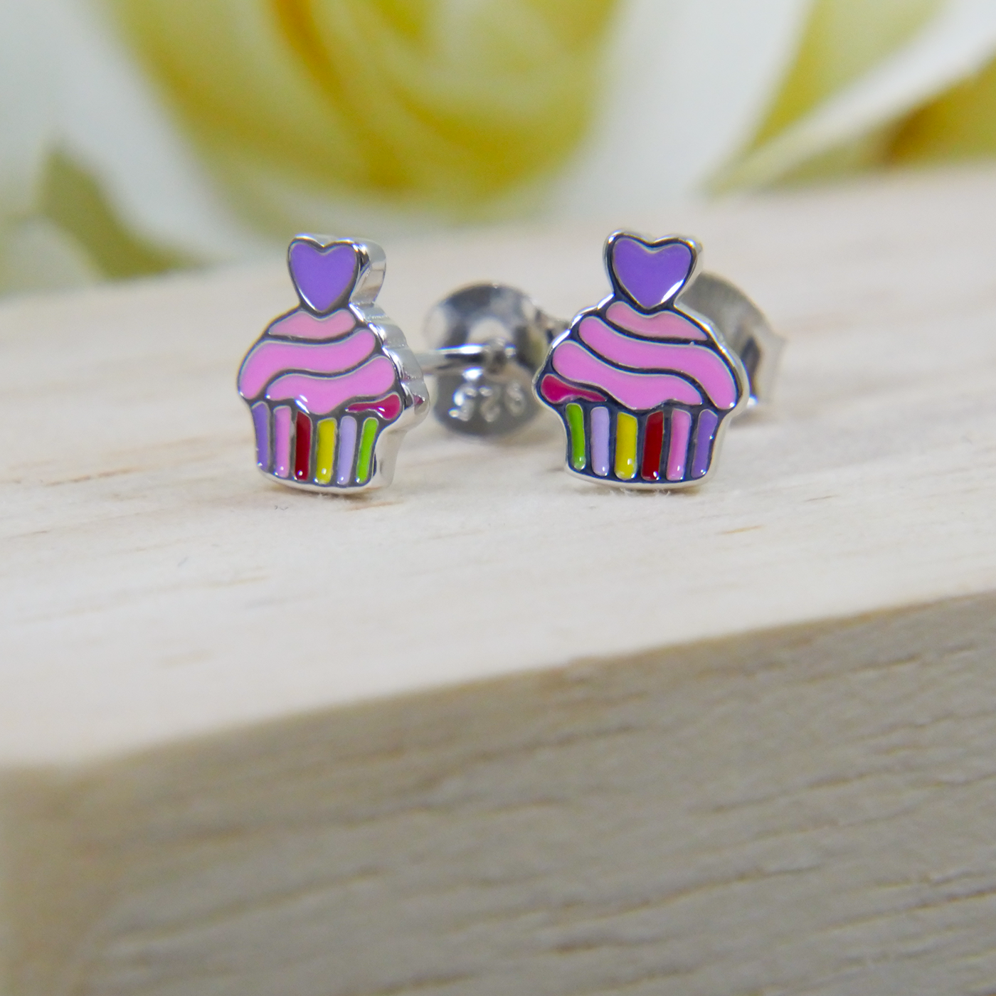 Cupcake-shaped earrings with colorful stripes on a wooden surface