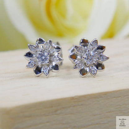 Silver flower-shaped earrings on a wooden surface with a blurred yellow rose in the background