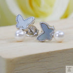 Butterfly-shaped earrings with white shell pearl stones on a wooden surface