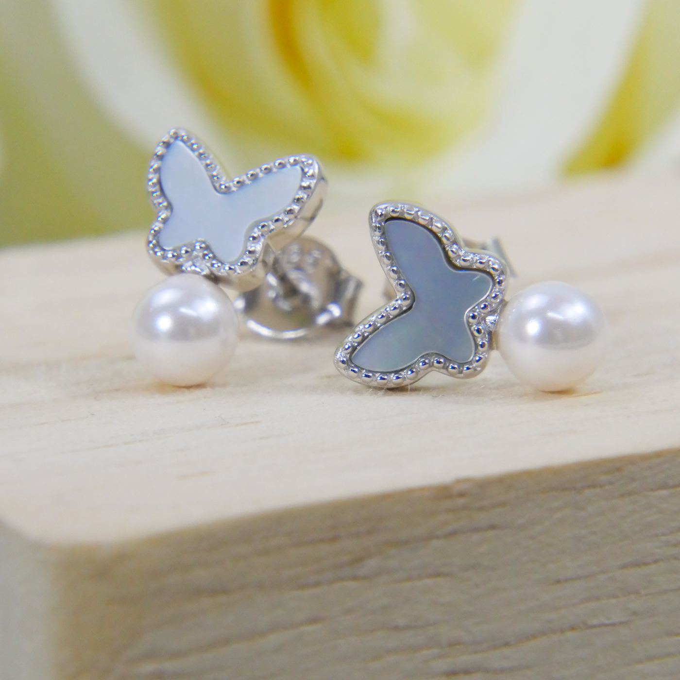 Butterfly-shaped earrings with white shell pearl stones on a wooden surface