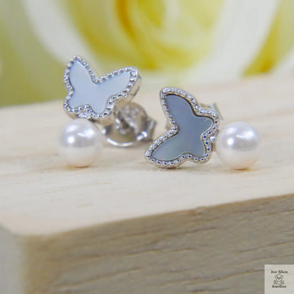 Butterfly-shaped earrings with white shell pearl stones on a wooden surface
