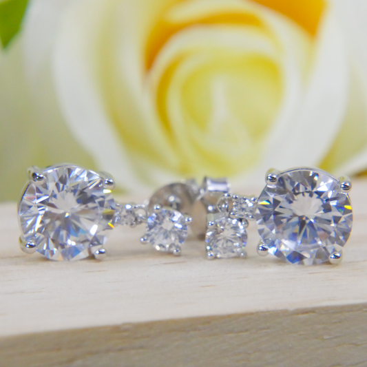 Set of Natural Zircon stud earrings on a wooden surface with a blurred rose background