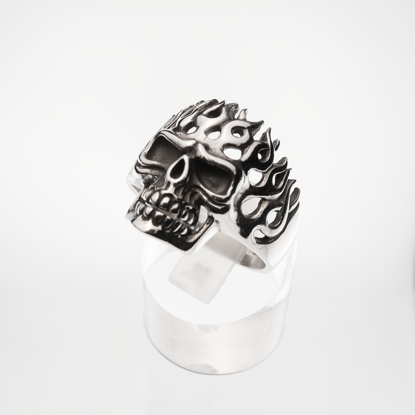 Silver skull ring with flame designs on a white background