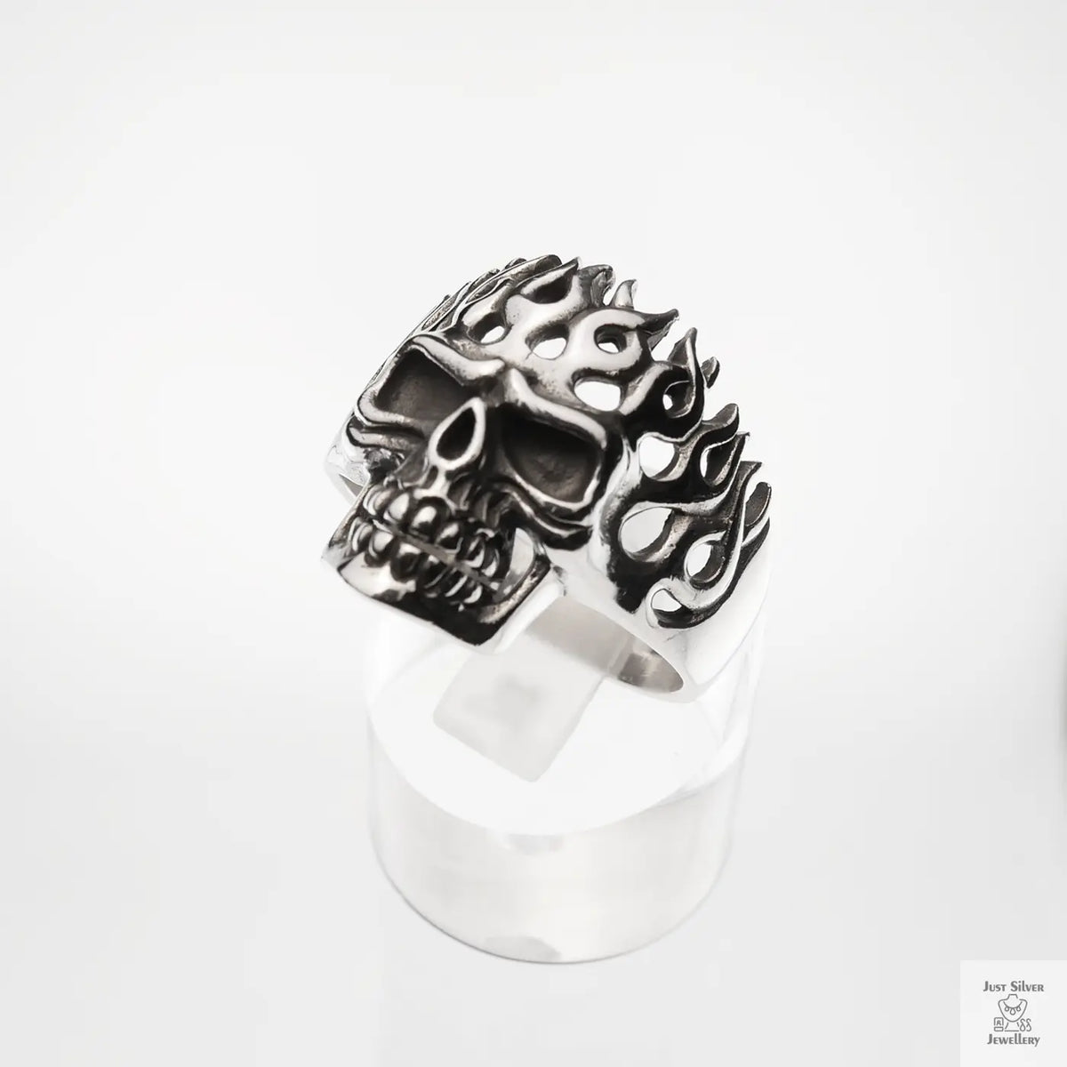 Silver skull ring with flame designs on a white background
