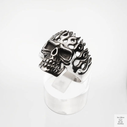 Silver skull ring with flame designs on a white background